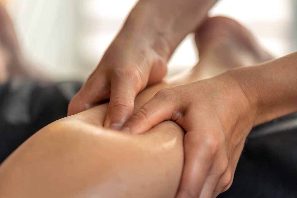 Close-up of a massage therapist applying pressure to a knee during therapy in a clinical setting